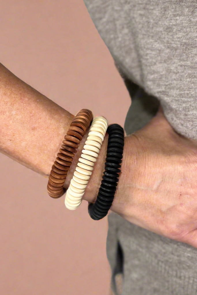 Model is wearing three chunky wood bangle bracelets.