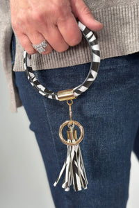 Model is holding a round zebra printed keychain wristlet. 