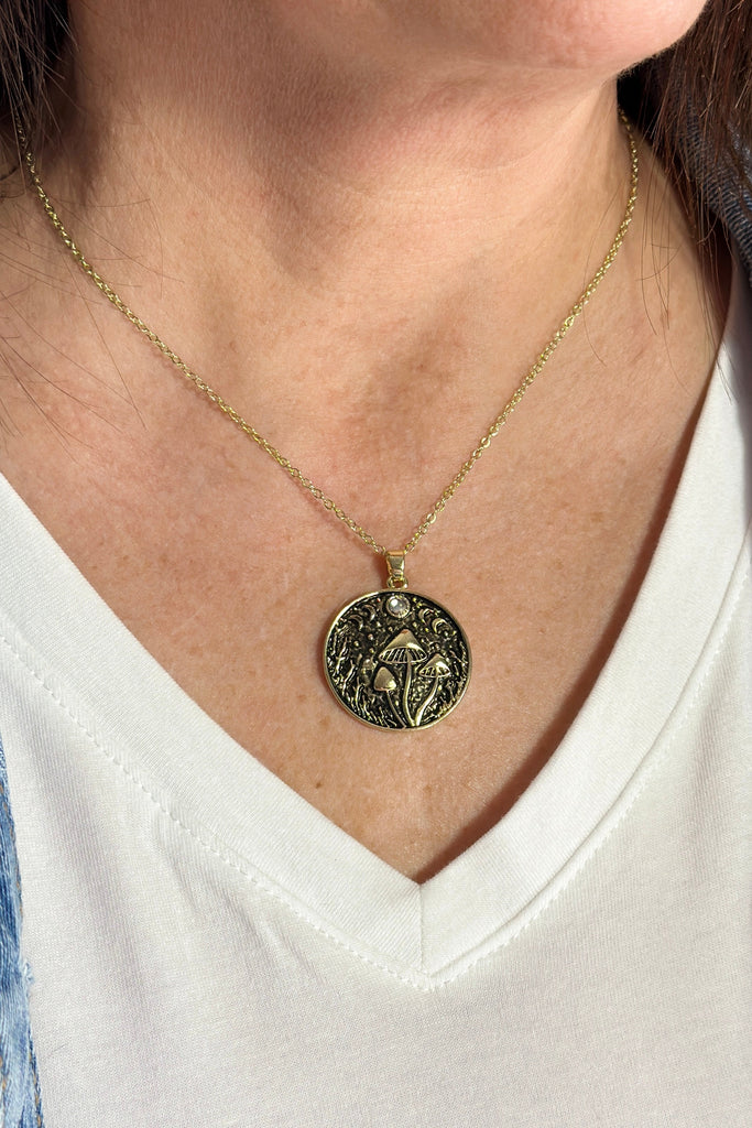 A gold pendant necklace. The pendant has toadstool mushrooms an moons features.