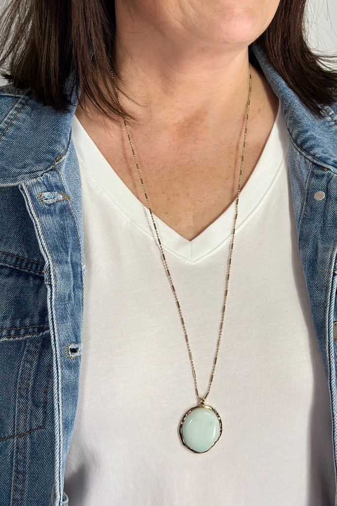 A long pendant necklace with a thin chain. he pendant is a mint colored circle.