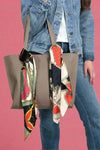 Model is showing off two silky patterned square scarves, that can be used to tie on purses or as neck scarves.