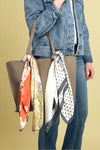 Model is showing off two silky printed scarfs that can serve as purse accessories or neck scarves. 