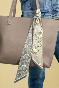 Model is showing off a twilly style floral scarf that can be used as a headband or bag tie.