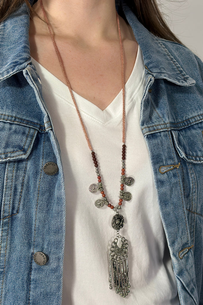 Model is wearing a long adjustable necklace that features beads and metal charms. 