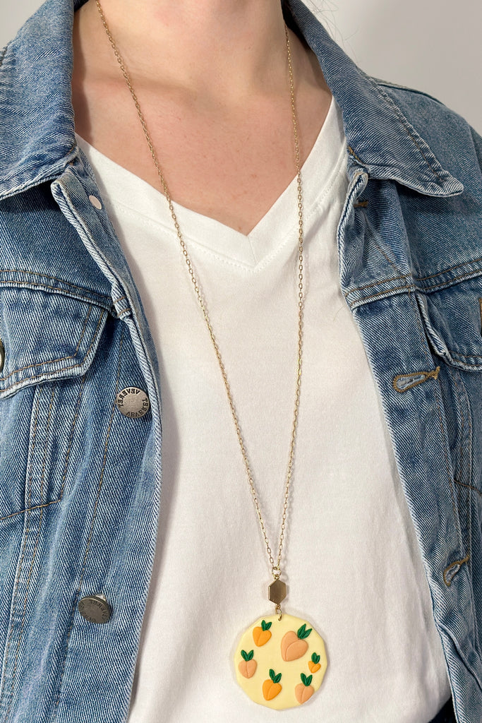 Model is wearing a long necklace with a clay round pendant. 