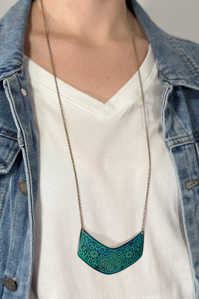 Model is wearing a long necklace with a stamped copper pendant. 