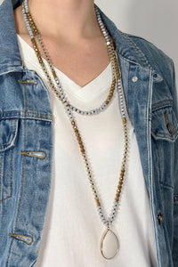 Model is wearing a beaded wrap necklace with a teardrop pendant. 