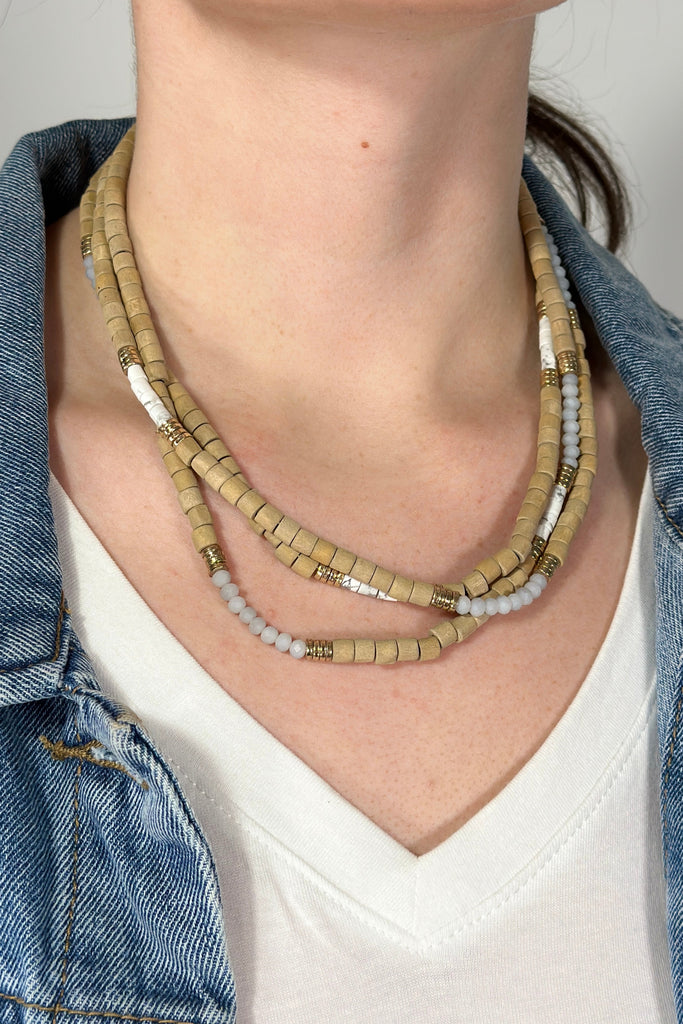 Model is wearing a layered collar length necklace with different types of beads. 