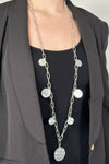 Model is wearing a long brushed silver chain link necklace that features hammered disc pendants. 