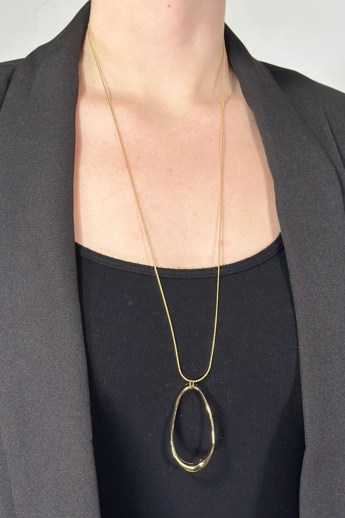 Model is wearing a long gold oval cutout pendant necklace.