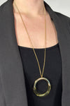 Model is wearing a long gold necklace with a circular shaped pendant. 