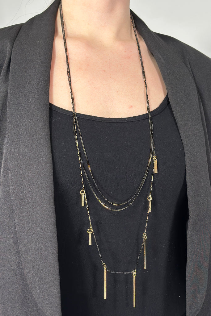 Model is wearing a black and gold layered necklace.