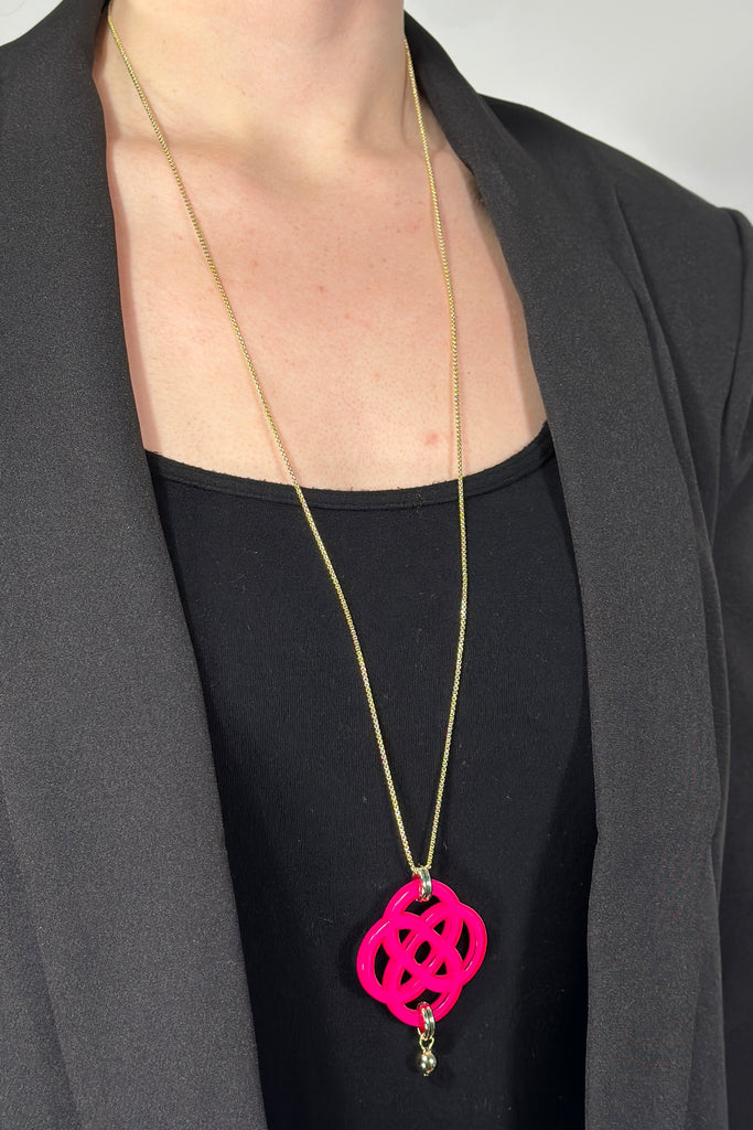 Model is wearing a long gold necklace with a hot pink acrylic pendant.