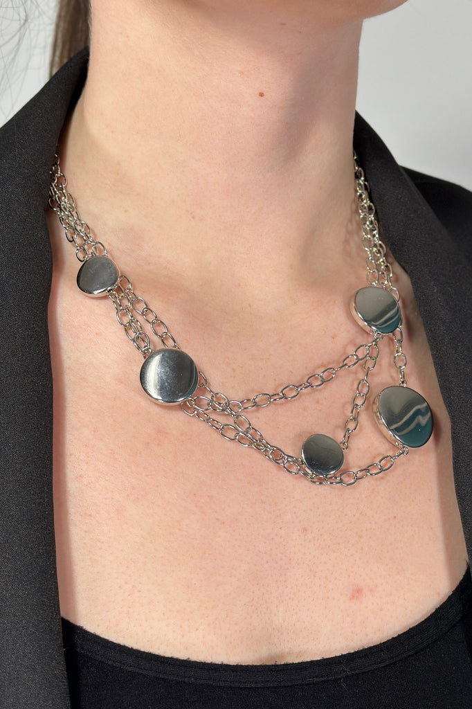 Model is wearing a silver chain necklace that features disk shaped beads. 