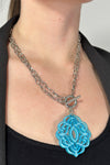 Model is wearing a silver chain necklace that features a blue acrylic pendant. 