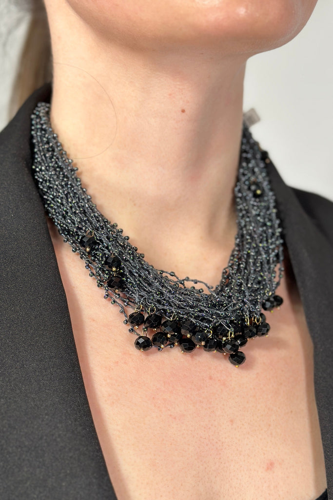 Model is wearing a short multi strand necklace that has extra small and medium sized beads. 