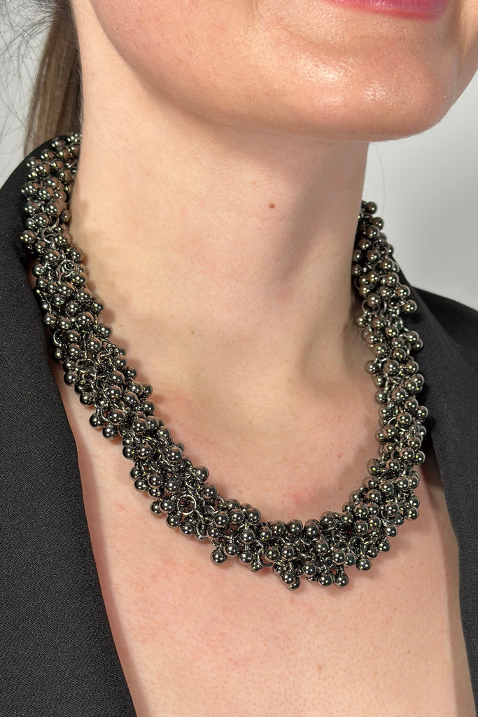 Model is wearing a collar length statement necklace with small shiny beads.