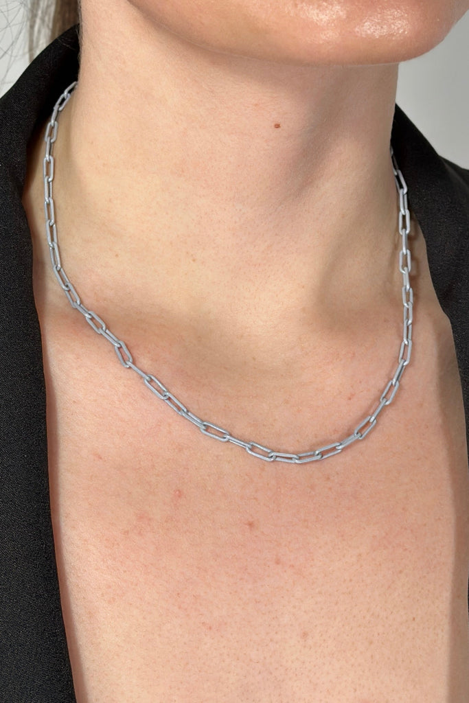 Model is wearing a small grey paper clip chain link necklace.