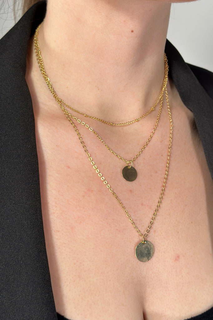 Model is wearing a gold chain 3-tier necklace with disc shaped pendants. 