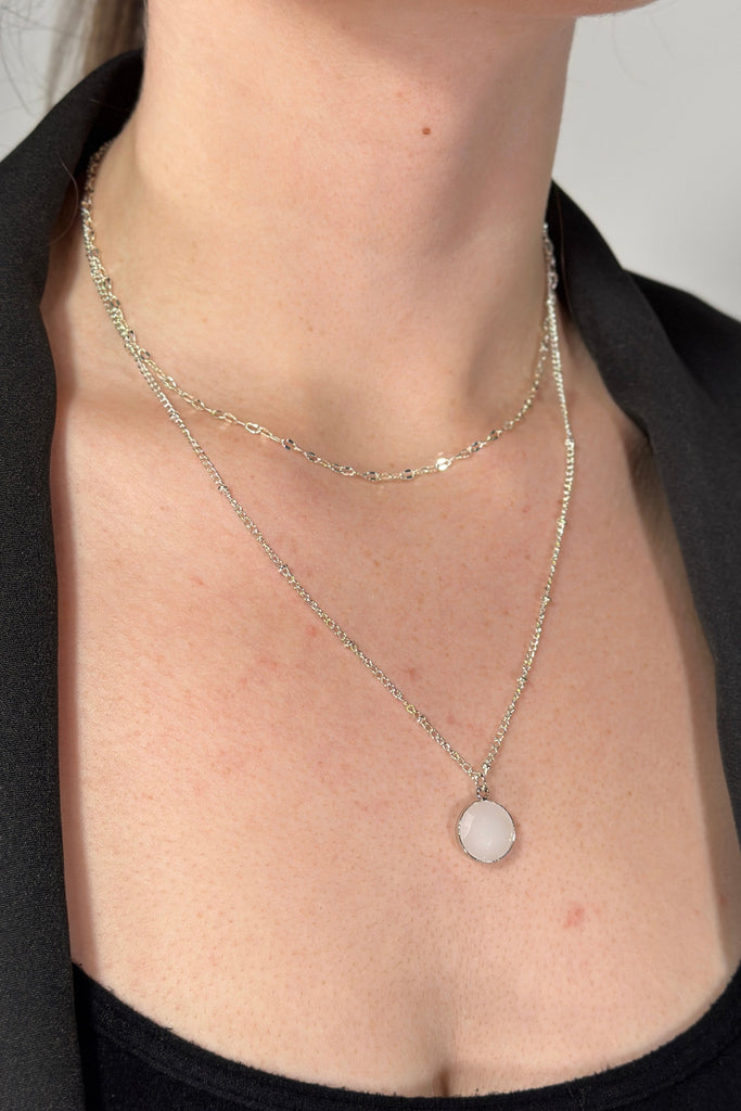 Model is wearing a silver 2-tier necklace with a small disc shaped pendant. 