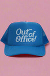 Light blue trucker hat with writing in white that reads “Out of Office!”.