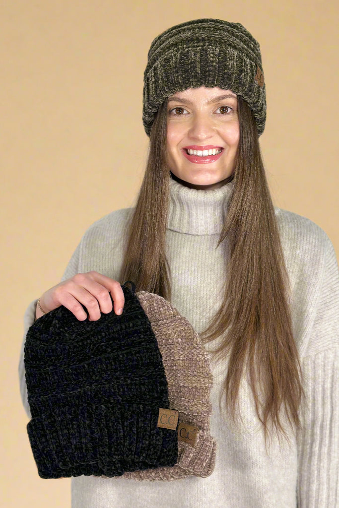 Model is wearing a chenille knit beanie in olive and holding two others in black and taupe. 