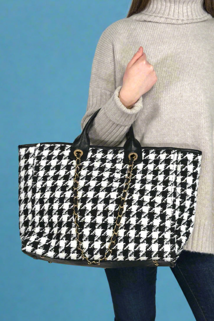 Model is holding a plaid tote bag with top handles and a shoulder strap.