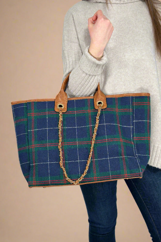 Model is holding a plaid tote bag with top handles and a shoulder strap.