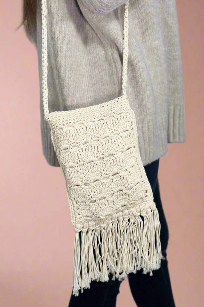 Model is wearing a crochet crossbody bag with fringe. 