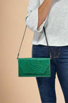 Model is holding a glossy faux snakeskin 3-1 clutch bag in a deep green color. 