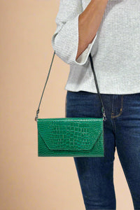 Model is holding a glossy faux snakeskin 3-1 clutch bag in a deep green color. 