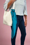 Model is showing off a satin teal colored square scarf tied on a purse.