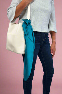 Model is showing off a satin teal colored square scarf tied on a purse.