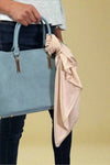 Model is showing off a champagne colored silk scarf that can be tied on purses.