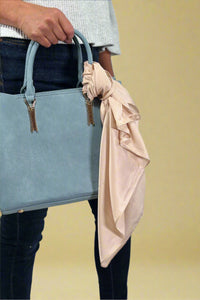 Model is showing off a champagne colored silk scarf that can be tied on purses.