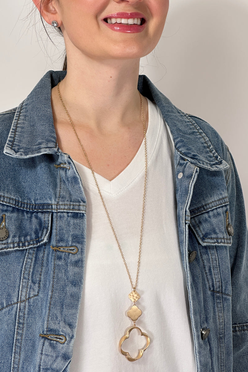 Model is wearing a long gold chain necklace with three different size clover pendants, going from smallest to largest. 