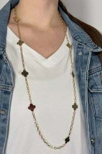 Model is wearing a long gold chain necklace with clover shaped pendants alternating throughout. 