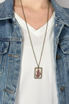 Model is wearing a long brass chain necklace with a pressed flower pendant. 