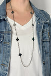 Model is wearing a long silver chain necklace with clover shaped pendants alternating throughout. 