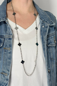 Model is wearing a long silver chain necklace with clover shaped pendants alternating throughout. 