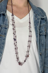 Model is wearing a long purple multi strand necklace that has purple beads throughout.