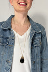 Model is wearing a long gold chain necklace with a teardrop shaped pendant that features rows of shiny small beads. 