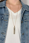 Model is wearing a long gold chain necklace with a vertical rectangle pendant made of Dalmatian jasper.