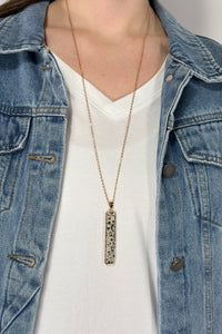 Model is wearing a long gold chain necklace with a vertical rectangle pendant made of Dalmatian jasper.