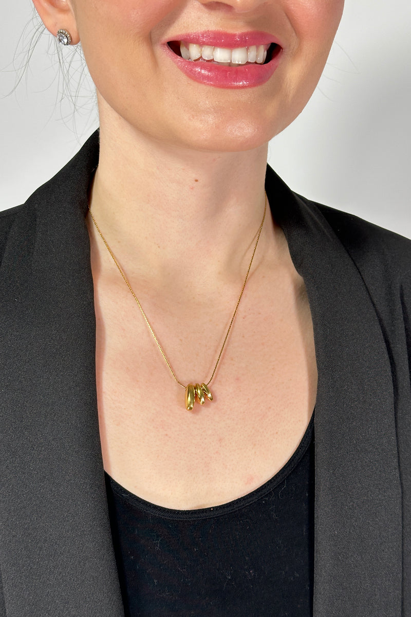Model is wearing a gold medium length necklace with three small oval shaped pendants. 