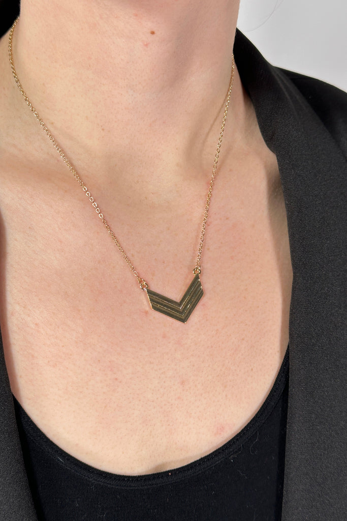 Model is wearing a collar length gold chain necklace that features a small arrow pendant. 