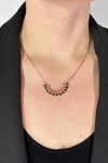 Model is wearing a collar length gold chain necklace that features a small black and pink beaded pendant. 