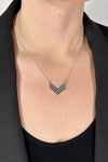 Model is wearing a collar length silver chain necklace that features a small arrow pendant. 