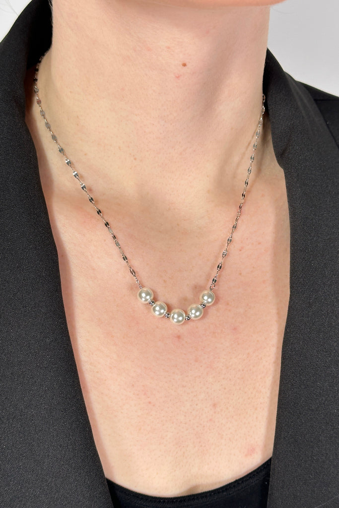 Model is wearing a collar length silver chain necklace that features a small row of five pearls. 