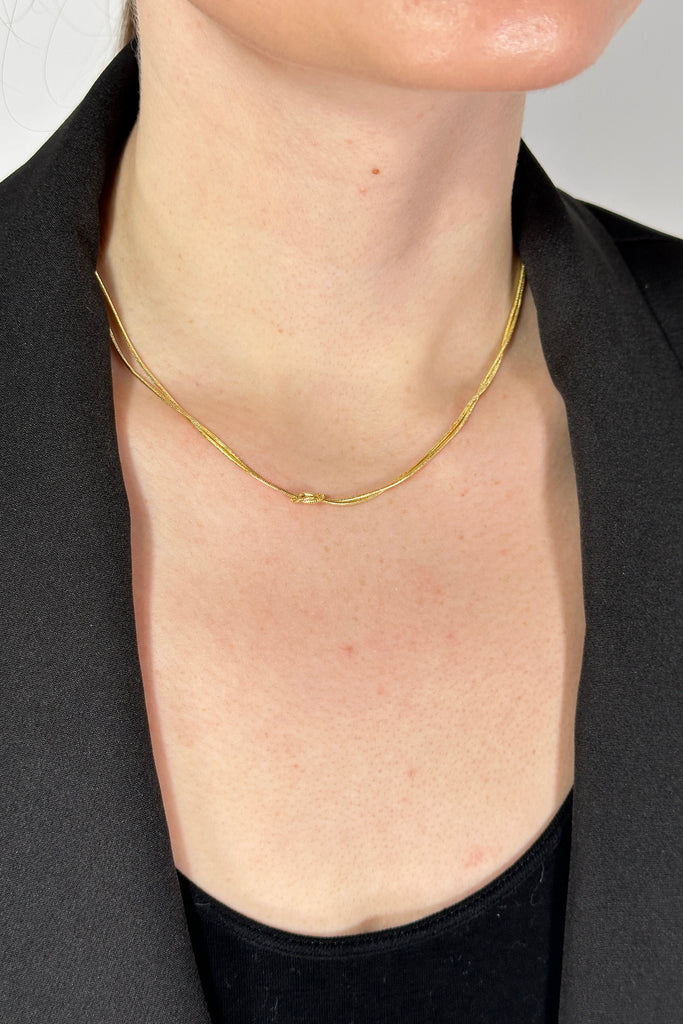 Model is wearing a dainty gold chain necklace with a small knot detail.